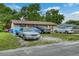 The beige home has an unkempt lawn with several vehicles parked, under a blue sky with scattered clouds at 2508 India Palm Dr, Edgewater, FL 32141