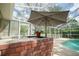 Outdoor brick kitchen area with umbrella, perfect for grilling and entertaining near the screened in pool at 5347 Pecan Rd, Ocala, FL 34472