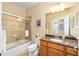 This bathroom features a shower-tub combo with glass doors, granite countertops, a decorative mirror, and wood cabinets at 7454 Sw 101St Ave, Ocala, FL 34481