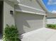 Attached garage showcasing the neutral door, exterior lighting, and manicured shrubbery at 80 Hickory Course Loop, Ocala, FL 34472