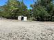 Lot featuring an outbuilding for storage or utility, surrounded by mature trees, gravel lot and blue skies at 5862 Sw 160Th Ct, Ocala, FL 34481