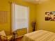 Bedroom with yellow walls, stripped bedding, white window sheers and a wicker side chair at 19480 Sw 100Th Loop, Dunnellon, FL 34432