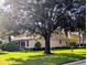 Side exterior of home on a verdant lawn, showing screened porch, manicured shrubbery, and a large shade tree at 2721 Day Lily Run, The Villages, FL 32162