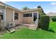 The back exterior with steps to an enclosed porch is shown on a green lawn next to trimmed foliage at 2721 Day Lily Run, The Villages, FL 32162
