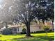 Side exterior of home on a verdant lawn, showing screened porch, manicured shrubbery, and a large shade tree at 2721 Day Lily Run, The Villages, FL 32162
