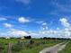 Scenic shot of a rural property with a dirt road, green pastures, clear sky, and some buildings in the distance at 4880 Bannon Island Rd, Haines City, FL 33844
