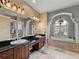 Bathroom showcasing dual sinks with dark countertops and a large soaking tub under an arched window at 221 Mclean Pt, Winter Haven, FL 33884