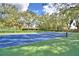 Beautifully maintained tennis court with a blue and green surface, surrounded by mature trees and a partial fence at 105 Wyndham Dr, Winter Haven, FL 33884