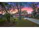 Charming home with a red-tiled roof, manicured lawn, mature trees, and inviting sunset sky at 128 Lake Ring Dr, Winter Haven, FL 33884