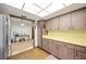A kitchen features wood cabinets, yellow countertops, and neutral flooring, leading into a carpeted bonus room at 660 Duggers Way, Lake Wales, FL 33859