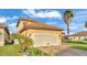 View of the home's side featuring a two-car garage, lush green lawn, and complemented by mature palm trees at 369 Villa Sorrento Cir, Haines City, FL 33844