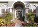 Welcoming home entrance featuring an arched doorway, decorative wreath, and colorful, mature landscaping at 7327 Bent Grass Dr, Winter Haven, FL 33884