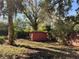 View of red shed nestled among trees and vegetation in backyard at 909 Spirit Lake Rd, Winter Haven, FL 33880
