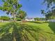 Green grass backyard view with large trees, partial view of a white house, and concrete parking area at 3736 Knights Station Rd, Lakeland, FL 33810