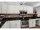 Close up of stainless appliances and granite counters complemented by white cabinets and mosaic backsplash at 2 Bridgewater Dr, Winter Haven, FL 33884