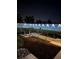 Outdoor night view of seating area, pavers, mulch, plants, enclosed with white vinyl fence lit by spotlights at 8243 Campbell Crossing Cir, Lakeland, FL 33810