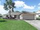Charming single-story home featuring a manicured lawn, complemented by swaying palm trees and a light neutral exterior at 1506 Chamberlain Loop, Lake Wales, FL 33853