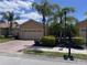Charming home featuring a brick driveway, a beige exterior, palm trees, and a two-car garage at 1224 Vienna Square Dr, Winter Haven, FL 33884