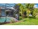 A picturesque backyard with a screened-in pool area, lush green landscaping, and tropical palm trees at 716 Maderia Ct, Kissimmee, FL 34758