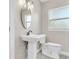 Bright bathroom featuring a pedestal sink, brushed faucet, oval mirror and white toilet at 333 Lake Otis Se Dr, Winter Haven, FL 33880