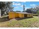 View of backyard featuring a small brick patio, green lawn, and the back exterior of the yellow single-story home at 1163 Lake Dr, Lake Wales, FL 33859