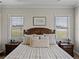 Bedroom featuring a wooden bed frame, neutral bedding, and two windows with scenic views at 3805 Mammoth Grove Rd, Lake Wales, FL 33898