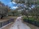A gravel driveway flanked by a black fence, leads through mature trees to a beautiful property at 3805 Mammoth Grove Rd, Lake Wales, FL 33898