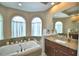 Bright bathroom featuring a soaking tub with tile surround, granite countertops, and three large arched windows at 2340 Pinehurst Ct, Davenport, FL 33837