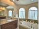 Elegant bathroom featuring a granite vanity, soaking tub, and arched windows that let in natural light at 2340 Pinehurst Ct, Davenport, FL 33837