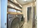 Laundry room with front loading washer and dryer, open shelving with decorative baskets, and beige tiled flooring at 2340 Pinehurst Ct, Davenport, FL 33837