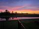 A scenic backyard view with a fence, showcasing a serene pond reflecting the vibrant sunset at 505 Adams View Ln, Auburndale, FL 33823
