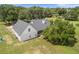 Aerial view of the rear of the white home with a large yard, black roof, and lush surrounding trees at 5820 E Johnson Ave, Haines City, FL 33844