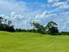 Scenic golf course view with lush green grass, mature trees, and a beautiful sky with puffy white clouds at 741 Canberra Rd, Winter Haven, FL 33884