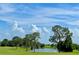 Scenic view of a golf course with a serene pond and mature trees under a beautiful blue sky with clouds at 741 Canberra Rd, Winter Haven, FL 33884