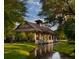 Idyllic covered bridge with stone columns and a tranquil stream surrounded by lush greenery at Red Tail at 25863 Crossings Bluff Ln, Sorrento, FL 32776