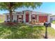 Charming single-story home with a well-maintained lawn, red accents, and mature tree providing shade at 411 Red Hawk Loop, Winter Haven, FL 33880