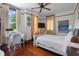 Cozy bedroom featuring ceiling fan, wooden floors, neutral curtains, and abundant natural light at 103 Se Tuscawilla Ave, Ocala, FL 34471