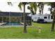 Backyard pool area with a screened-in enclosure, lush grass, palm trees, and an RV in the background at 217 Shore Loop, Winter Haven, FL 33884