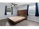 Bedroom with wood-look floors, platform bed, ceiling fan, and two windows with blue curtains at 1107 Linmar Ave, Fruitland Park, FL 34731