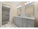 Bright bathroom featuring double sinks, grey cabinets, framed mirrors, and a walk-in shower with tiled surround at 144 Pinewood Cir, Kissimmee, FL 34743