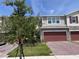 Townhome exterior with red garage door, stone accents, and brick driveway, framed by mature landscaping at 1258 Wispy Cypress Drive Dr, Kissimmee, FL 34746