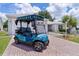 Close-up of a blue golf cart parked on a brick paver driveway with a well-kept lawn and landscaping at 1305 Guerra Ave, The Villages, FL 32159