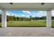 An outdoor view of a covered back porch with a brick floor that overlooks the lush green lawn and a pond with trees beyond at 6066 Arbor Watch Loop, Orlando, FL 32829