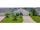 Landscaped front yard featuring lush lawn, decorative trees and shrubbery leading to a gray home with a two car garage at 924 Figwood Loop, The Villages, FL 32163