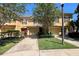 A daytime exterior shot of a two-story tan townhome featuring manicured lawn, trees, and a sidewalk at 721 Interlude Ln # 105, Orlando, FL 32824