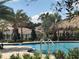 Resort-style swimming pool with clear blue water, surrounded by lush palm trees, and a charming thatched roof cabana at 1077 Quaker Ridge Ln, Davenport, FL 33896