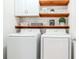 Bright laundry room featuring modern machines, wooden shelving, and charming decor at 6144 Forest Ridge Way, Winter Haven, FL 33881
