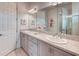 Bright bathroom featuring dual sinks, gray cabinets, white tile floors, and a large mirror at 2285 Palm Tree Dr, Kissimmee, FL 34759