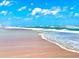 Beautiful beach with soft sand meeting gentle waves under a bright blue sky with scattered clouds at 306 Hang Loose Way, Daytona Beach, FL 32124