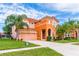 Two-story house with orange stucco and a tile roof, featuring palm trees and a landscaped yard at 4525 Stella St, Kissimmee, FL 34746